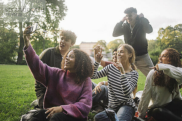 Fröhliches Teenager-Mädchen  das im Park ein Selfie mit männlichen und weiblichen Freunden per Smartphone macht