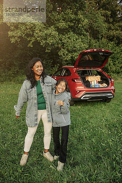 Lächelnde Frau  die Spaß mit ihrer Tochter hat  die neben dem Auto im Park steht