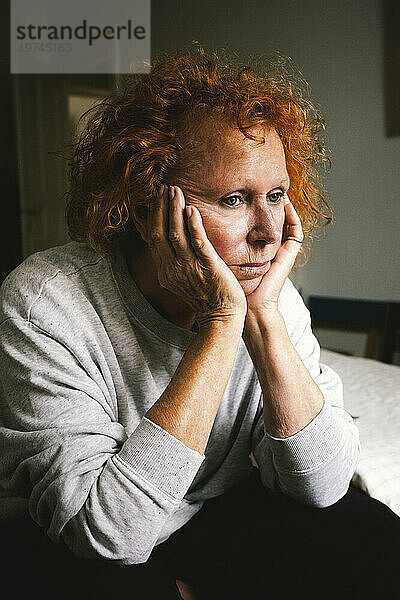 Nachdenkliche  deprimierte ältere Frau sitzt mit dem Kopf in den Händen zu Hause