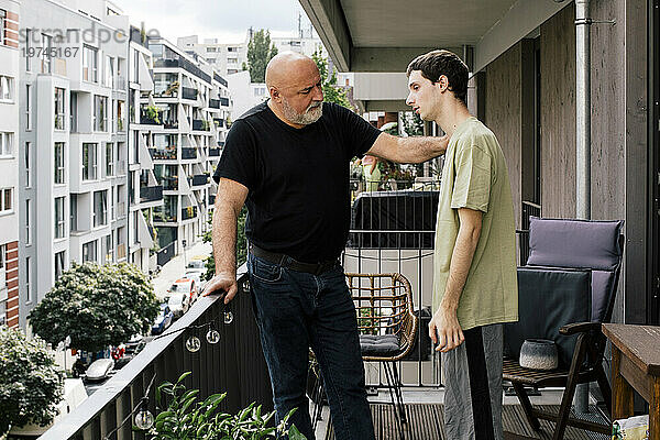 Reifer Mann tröstet deprimierten Sohn  der auf dem Balkon steht