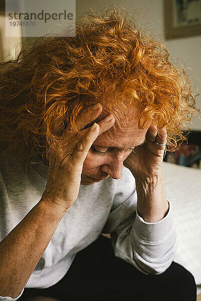 Deprimierte rothaarige ältere Frau sitzt mit dem Kopf in den Händen auf dem Bett