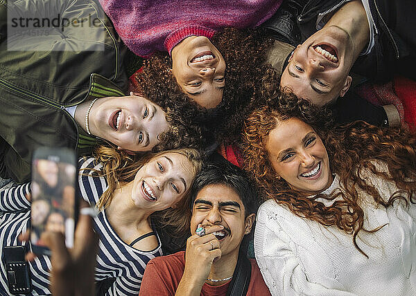 Hand einer nicht wiederzuerkennenden Person  die fröhliche Teenager-Freunde fotografiert  die Spaß haben  während sie sich im Park hinlegen
