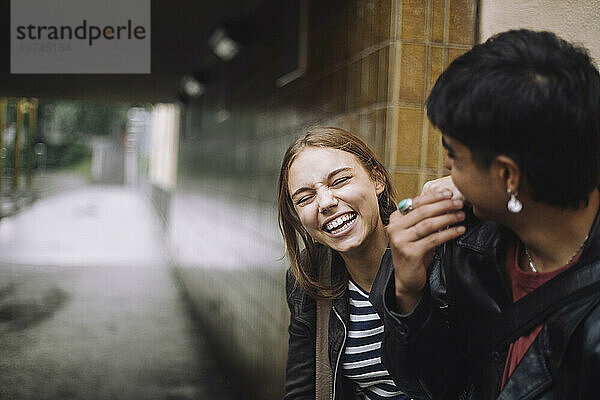 Fröhliches Mädchen lacht mit jugendlichem Freund an der Wand