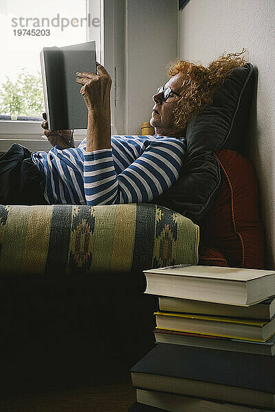 Seitenansicht einer älteren Frau  die ein Buch liest  während sie zu Hause im Bett liegt