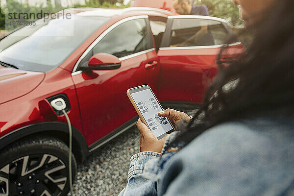 Frau nutzt mobile App auf Smartphone in der Nähe eines Elektroautos