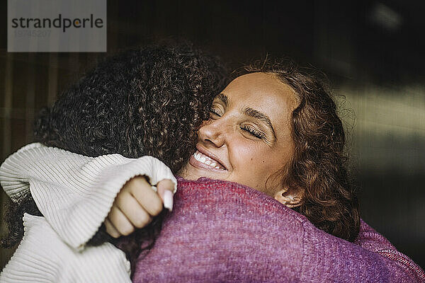 Lächelndes Teenager-Mädchen mit geschlossenen Augen umarmt ihre Freundin