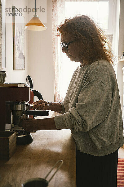 Seitenansicht einer älteren Frau  die zu Hause in der Küche Kaffee kocht