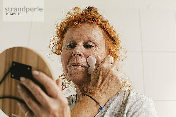 Ältere Frau schaut in den Spiegel und massiert ihr Gesicht an der Wand