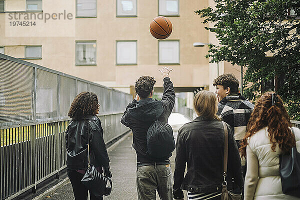 Teenager wirft Basketball  während er mit Freunden auf dem Fußweg spaziert