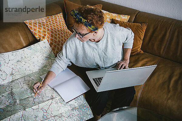 Seitenansicht einer älteren Frau  die eine Reise auf der Karte plant und zu Hause einen Laptop benutzt