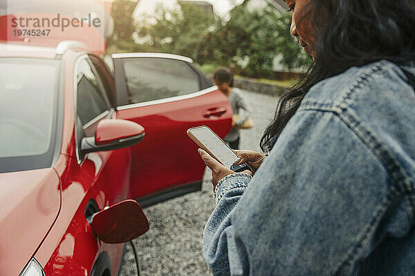 Frau benutzt Smartphone neben Elektroauto