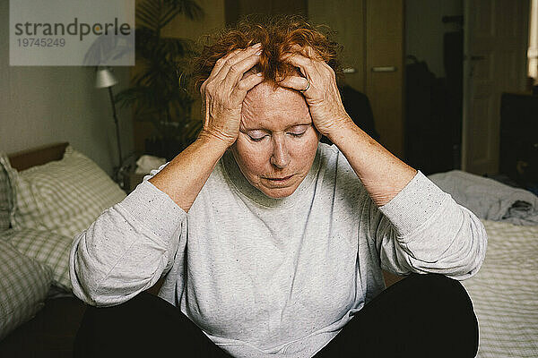 Deprimierte ältere Frau sitzt mit dem Kopf in den Händen im Schlafzimmer