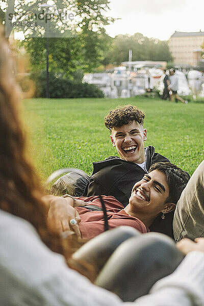 Fröhliche männliche Freunde lachen zusammen  während sie mit einem Freund im Park reden