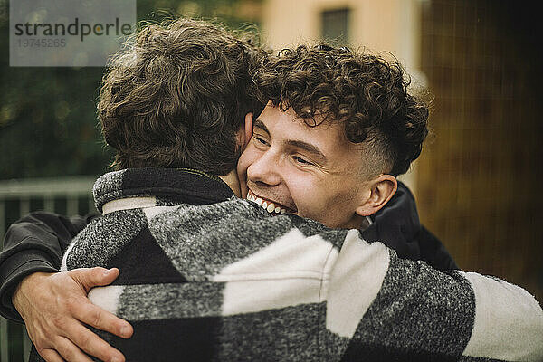 Fröhlicher Junge mit lockigem Haar umarmt seinen männlichen Freund im Flanellhemd