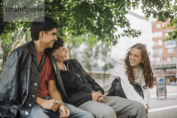 Männliche und weibliche Teenager-Freunde lachen zusammen  während sie auf einer Bank sitzen