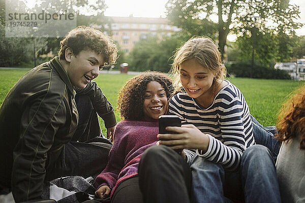 Neugieriges Teenager-Mädchen teilt Smartphone mit männlicher und weiblicher Freundin im Park