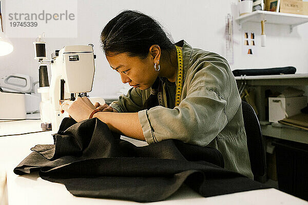 Konzentrierte Näherin näht Kleidung mit Nähmaschine  während sie im Geschäft arbeitet