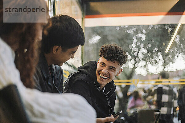 Fröhlicher Junge lacht mit Freunden  während er an der Bushaltestelle sitzt