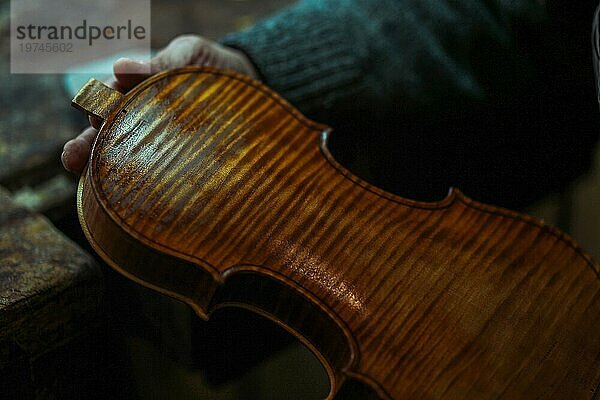 Ein erfahrener Geigenbauer hält ein frisch lackiertes Instrument in seinen Händen in Cremona  Italien  Makro Nahaufnahme  selektiver Fokus  Bokeh  Europa