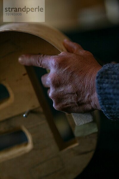 Luthier handwerklichen Geigenbauer faltige Hand halten schnitzen sculpt Meißel Rippen eines neuen klassischen Modells Cello in der Werkstatt Cremona Italien  selektiver Fokus  Bokeh