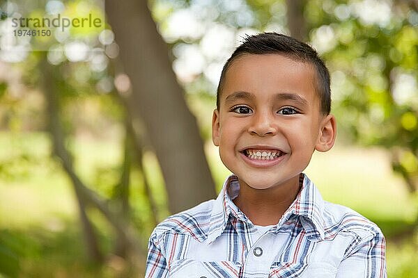 Lächelnder junger hispanischer Junge im Freien unter den Bäumen