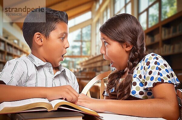 Zwei hispanische Schulkinder in einer Bibliothek mit einem schockierten Gesichtsausdruck