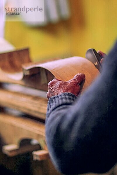 Die faltigen Hände des Geigenbauers schnitzen die Rippen eines neuen klassischen Cellomodells in der Werkstatt in Cremona  Italien  selektiver Fokus  Bokeh  Europa