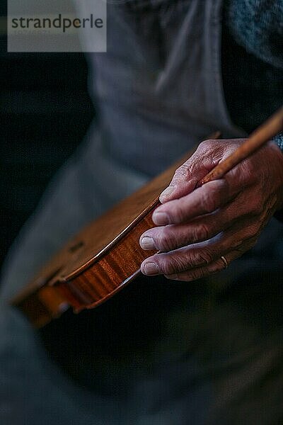 Senior Experte Geigenbauer Geigenbauer tragen Schürze halten klassische handgefertigte Geige malen natürlichen Zutaten Rezept in Cremona Italien Heimat der besten Handwerker dieser Art