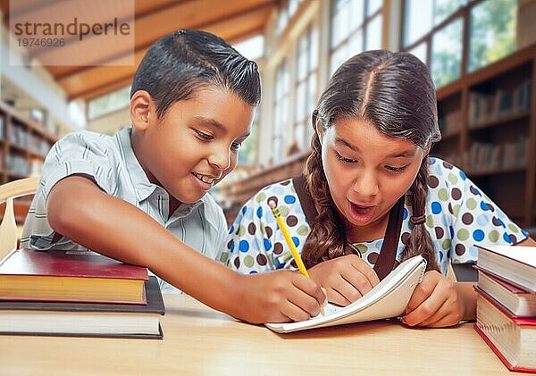Zwei hispanische Schulkinder in einer Bibliothek  die sich über ihre Hausaufgaben freuen