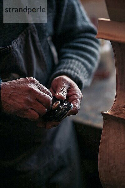 Älterer Geigenbauer mit faltigen alten Händen hält einen Meißel in einer Werkstatt in Cremona  Italien  selektiver Fokus  Bokeh  Europa