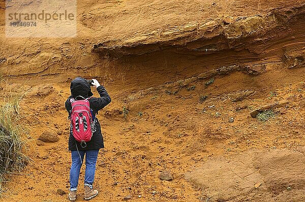 Frau  Wanderin mit Rucksack fotografiert  rötlicher Felsen aus Limonit  Geotop Morsum-Kliff  Morsum  Nordseeinsel Sylt  Nordfriesland  Schleswig-Holstein  Deutschland  Europa