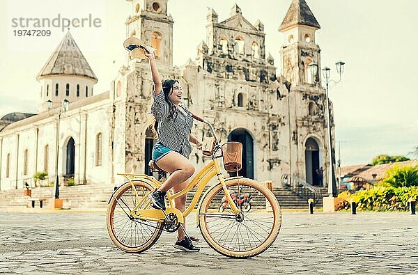 Lifestyle eines glücklichen Mädchens auf dem Fahrrad mit Hut auf der Straße. Glückliche junge Frau mit Hut auf dem Fahrrad auf der Straße. Granada  Nicaragua. Tourismuskonzept