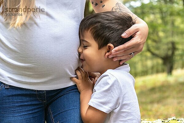 Zartes Bild eines Kindes  das den Bauch seiner schwangeren Mutter im Freien umarmt