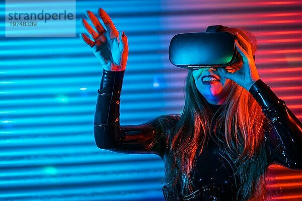 Glückliche Frau mit Virtual Reality Brille in einem futuristischen Raum bei Nacht mit Neonlicht