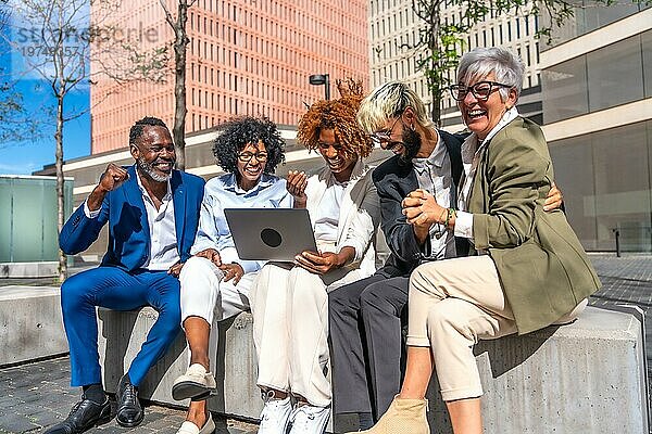 Fröhliche Gruppe multiethnischer Geschäftsleute mit Laptop auf einer Bank im Freien sitzend
