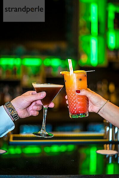 Vertikale Nahaufnahme von zwei Personen  die mit Luxus Cocktails in einer Bar anstoßen