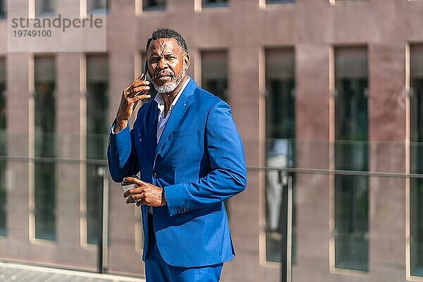 Afrikanischer reifer Geschäftsmann  der im Freien mit dem Mobiltelefon spricht  während er einen Kaffee zum Mitnehmen trinkt