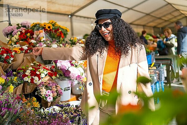 Glückliche lateinische Frau wählt Blumen in einem Blumenladen im Freien auf einem Straßenmarkt an einem sonnigen Wintertag aus