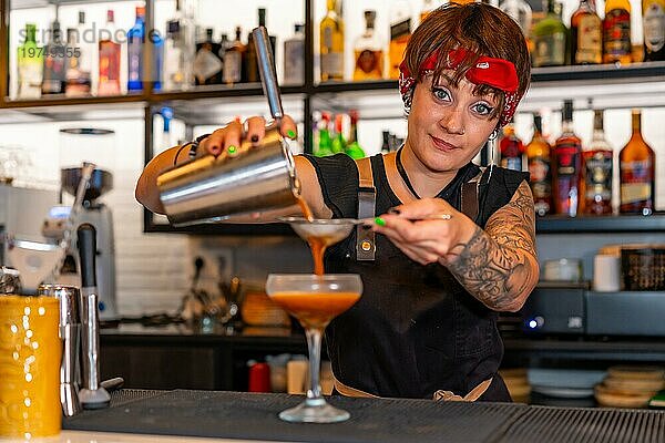 Glücklicher Barkeeper  der einen Cocktail aus dem Shaker in ein Cocktailglas am Tresen einer Bar gießt