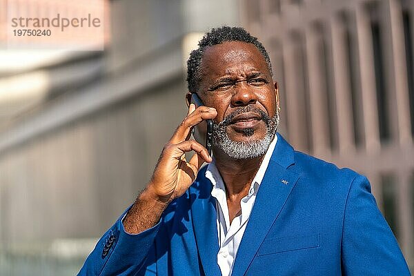 Älterer afrikanischer Geschäftsmann im blauen Anzug  der im Freien telefoniert