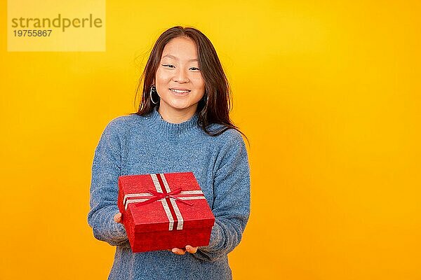 Studiofoto mit gelbem Hintergrund einer chinesischen Frau  die ein Geschenk überreicht und in die Kamera lächelt