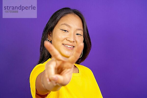 Studio Foto mit lila Hintergrund einer chinesischen Frau gestikulieren Sieg lächelnd in die Kamera