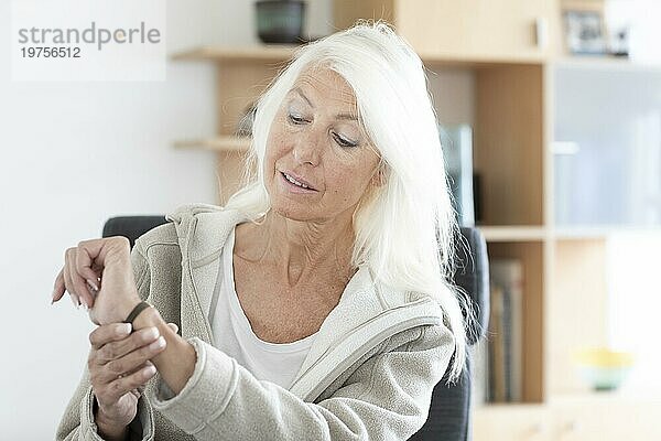 Ältere Frau mit langen Haaren schaut auf Armbanuhr zu Hause