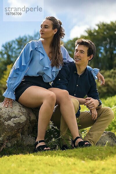Vertikales Foto eines stilvollen jungen Paares  das auf dem Berg sitzend zur Seite schaut