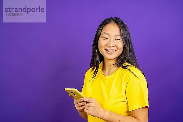 Studio Foto mit lila Hintergrund einer chinesischen Frau mit Telefon und lächelnd in die Kamera