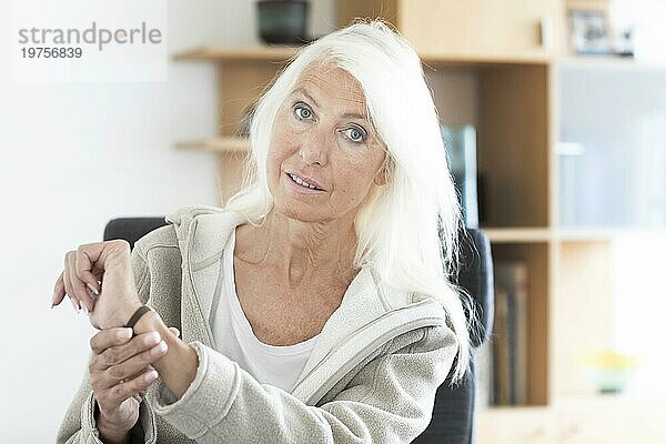 Ältere Frau mit langen Haaren schaut auf eine Armbanduhr zu Hause