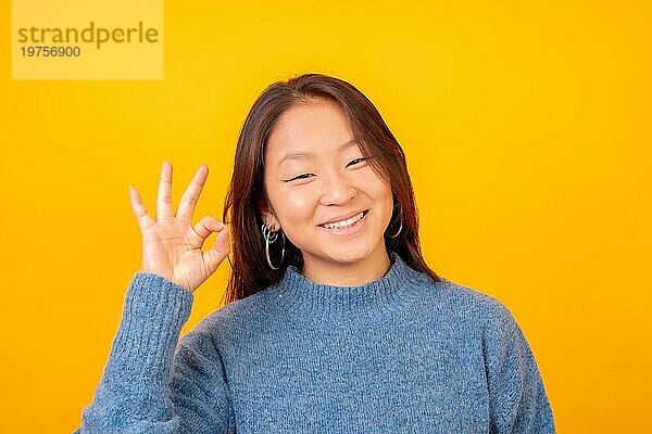Asiatische Frau  die kühl und wunderbar in die Kamera schaut  auf einem gelben Hintergrund