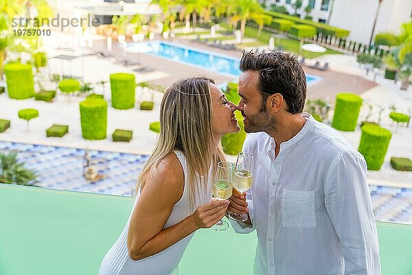 Ein frisch verheiratetes Paar küsst sich  während es mit Champagner auf der Terrasse eines Luxushotels anstößt