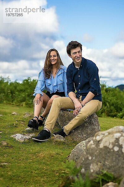 Vertikales Foto eines jungen Paares  das auf einem Felsen im Gebirge sitzt