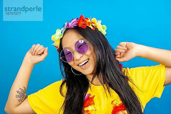 Studiofoto mit blauem Hintergrund von einer tanzenden Chinesin mit Sonnenbrille und hawaiianischer Blumenkrone